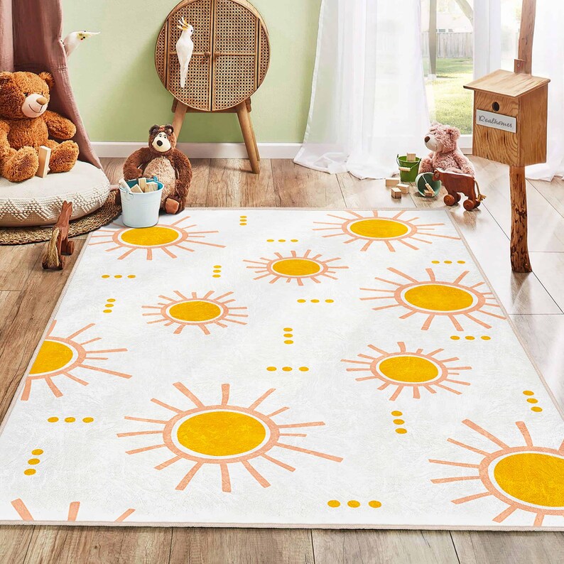 May include: White rectangular area rug with a repeating pattern of yellow and peach suns. The rug is designed for a child's room, with a soft, playful aesthetic. The suns are stylized and evenly spaced across the rug's surface.
