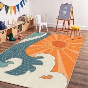 Könnte beinhalten: Rechteckiger Teppich mit einem stilisierten Design, das eine große orangefarbene Sonne und eine blaue Welle zeigt. Der Teppich hat einen cremefarbenen Hintergrund und besteht wahrscheinlich aus einem weichen Material. Der Teppich liegt in einem Raum mit Holzboden.