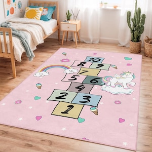 Può includere: Un tappeto rettangolare rosa per bambini con una griglia di campana numerata da 1 a 10. Il tappeto presenta un arcobaleno, un unicorno, coni gelato, cuori e ciambelle. Ideale per la cameretta o la sala giochi di un bambino.
