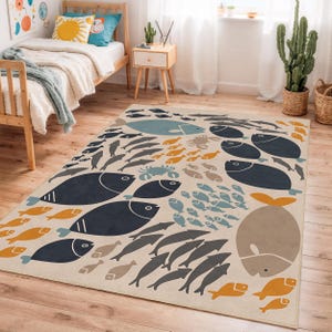 Puede incluir: Alfombra beige con un diseño de vida marina. La alfombra presenta ilustraciones estilizadas de peces en tonos azul marino, naranja, gris y azul. También se representa una ballena grande y un cangrejo. La alfombra está colocada sobre un suelo de madera.