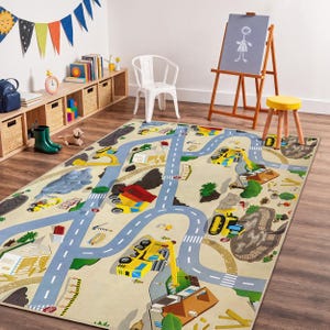 Può includere: Tappeto gioco beige per bambini con un design stradale e di veicoli da cantiere. Il tappeto presenta strade blu, veicoli da cantiere gialli e illustrazioni di edifici e alberi. Il tappeto è posizionato su un pavimento in legno in una sala giochi.