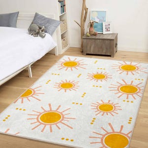May include: A rectangular white rug with a repeating pattern of orange and yellow suns. The rug is placed on a wooden floor in a room with a bed and a wooden chest. The suns have a playful, cartoonish design.