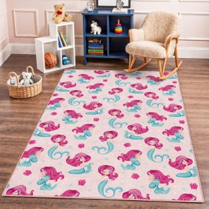 May include: A rectangular pink rug featuring a repeating pattern of mermaids. Each mermaid has long pink hair and a turquoise tail and top. Coral and star accents are scattered across the rug's surface. The rug is designed for a child's room.