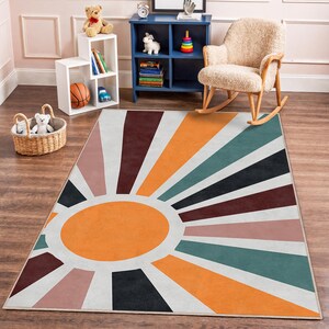 May include: A rectangular rug with a retro sunburst design. The rug features an orange oval in the centre with radiating stripes in shades of orange, teal, black, brown, pink, and white. The rug is placed on a wooden floor.