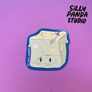 May include: A die-cut sticker featuring a cartoon cube with a face, a sword, and other small icons. The sticker has the text "ALWAYS HUNGRY" and "SILLY PANDA STUDIO" on a purple background.