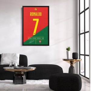 K&ouml;nnte beinhalten: Gerahmtes Poster mit dem Namen "RONALDO" in gelber Schrift &uuml;ber der Zahl "7" auf rotem und gr&uuml;nem Hintergrund. Die Worte "PORTUGAL NATIONAL FOOTBALL TEAM" stehen unter der Zahl. Enth&auml;lt eine Unterschrift und das Logo des portugiesischen Fu&szlig;ballverbands.