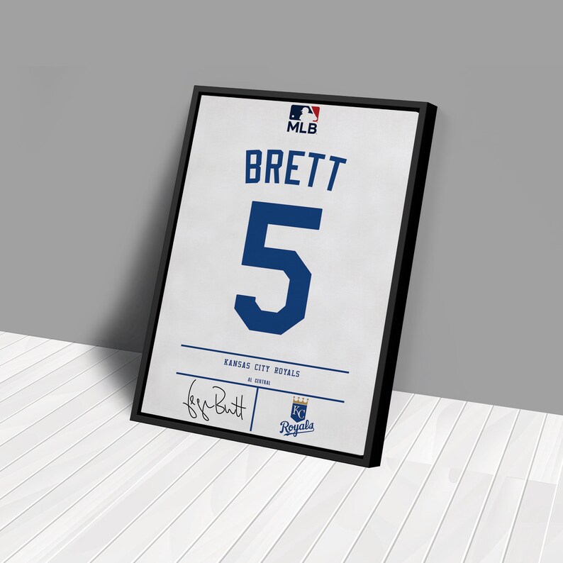 May include: Framed print of a Kansas City Royals baseball jersey. The jersey features the name "BRETT" and the number "5" in blue on a white background. Includes the MLB logo and the team logo.
