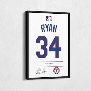 May include: Framed white baseball jersey featuring the name "RYAN" and the number "34" in blue and red. The MLB logo is at the top, with "TEXAS RANGERS" and a signature at the bottom. The jersey is in a black frame.