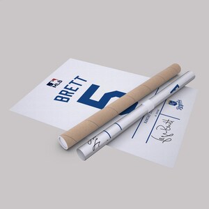 May include: A white poster with the name "BRETT" and the number "5" in blue, along with a rolled-up poster and a tube. The MLB logo is visible. The rolled poster has the signature "George Brett".
