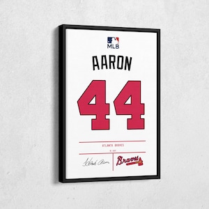 May include: A framed print of a baseball jersey. The jersey is white with the name "AARON" and the number "44" in red. The MLB logo is at the top. The Atlanta Braves logo and signature are at the bottom.