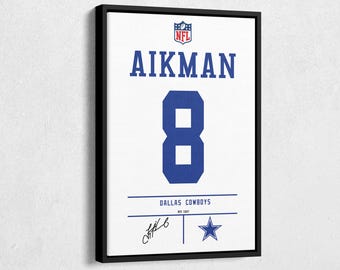 Puede incluir: Impresión enmarcada de una camiseta de los Dallas Cowboys con el nombre "AIKMAN" y el número "8" en azul sobre un fondo blanco. Incluye el logotipo de la NFL y el nombre del equipo. La impresión está en un marco negro.