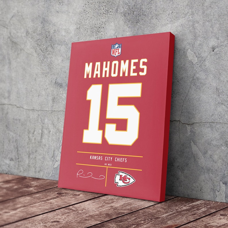 May include: A red canvas print featuring the name "MAHOMES" and the number "15" in white. The print also includes "KANSAS CITY CHIEFS" and a team logo. The NFL logo is visible in the top corner. The canvas is leaning against a gray wall on a wooden surface.