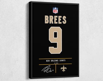 以下が含まれることがあります： 黒いフレームに入ったジャージプリント。名前は「Brees」、番号は「9」で金色。NFLのロゴが上部にあり、「New Orleans Saints」と署名が下部にあります。フルール・ド・リスのエンブレムも表示されています。