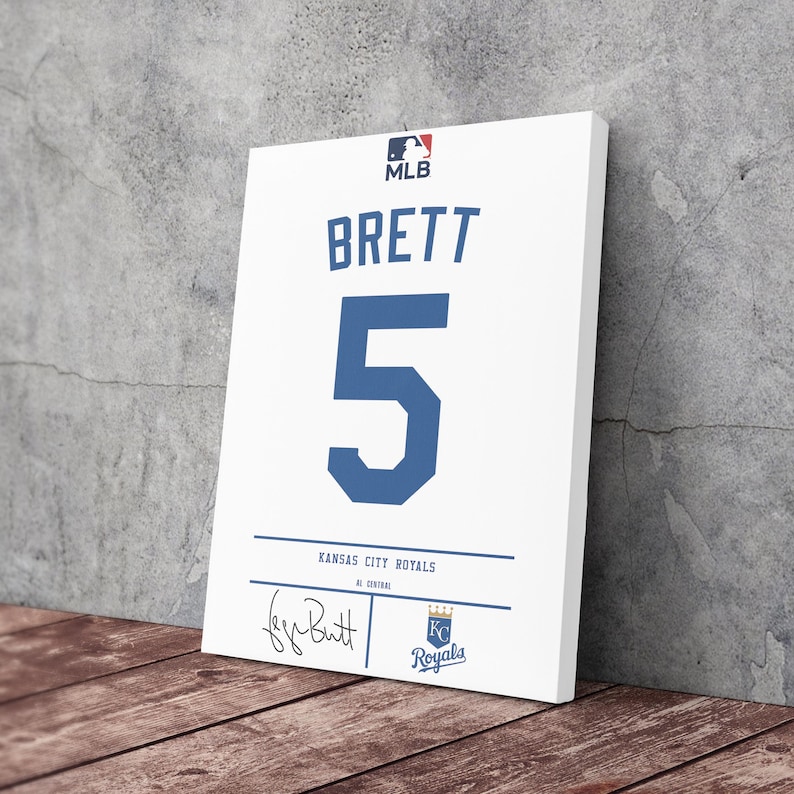 May include: White canvas art print of a baseball jersey. The jersey features the name "BRETT" and the number "5" in blue. The MLB logo is at the top, with "Kansas City Royals" and a signature at the bottom.