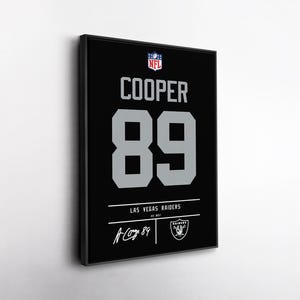 May include: Framed black and silver Las Vegas Raiders jersey featuring the name "COOPER" and the number "89". Includes the NFL logo, team logo, and player signature. A decorative piece for sports fans.