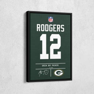 May include: Framed artwork of a Green Bay Packers jersey design. The jersey shows "RODGERS" above the number "12" in white. The team logo and signature are also visible. The background is green.