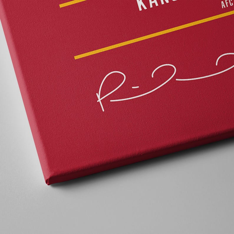 May include: A red canvas print with white text and a signature-style design. The text includes the word "KANSAS" and the letters "AFC". Yellow horizontal lines are present. The canvas is angled, showing its textured surface.
