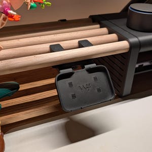Könnte beinhalten: Ein schwarzer Schreibtisch-Organizer mit Holzdübeln und einer schwarzen Ablage. Auf der Ablage sind die Buchstaben "W+" geprägt. Der Organizer steht auf einem weißen Schreibtisch mit farbenfrohen Dekorationsgegenständen.