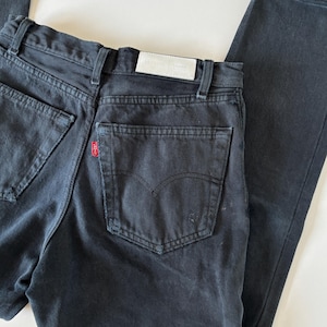 May include: Dark wash denim jeans with a classic five-pocket design. The jeans feature a red logo tag on the back pocket and a white label on the waistband. The jeans have a straight leg cut and a faded appearance.