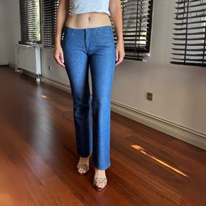 May include: Blue denim jeans with a slight flare at the bottom. The jeans have a classic five-pocket design and a mid-rise waist. The denim has a medium wash and a subtle texture. The jeans are a versatile wardrobe staple.