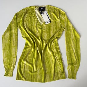 May include: A long-sleeved, lime green sweater with a V-neck. The sweater has a vertical striped pattern and a tag that reads "D&G". The garment is made of a soft, lightweight material.