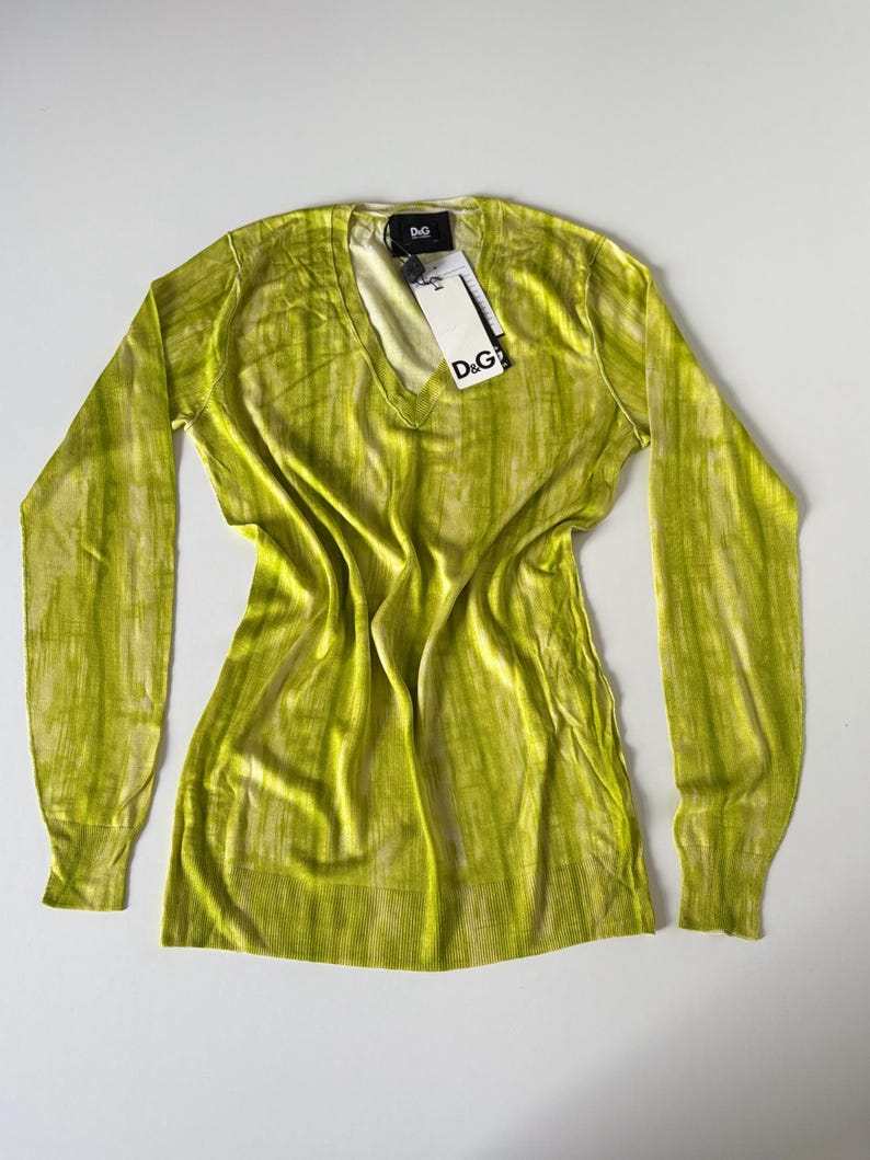 May include: A long-sleeved, lime green sweater with a V-neck. The sweater has a vertical striped pattern and a tag that reads "D&G". The garment is made of a soft, lightweight material.