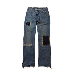 May include: Light blue denim jeans with two dark blue patches and a distressed knee. The jeans have a classic five-pocket design and a straight leg fit. The hem is frayed. A casual, everyday wear item.