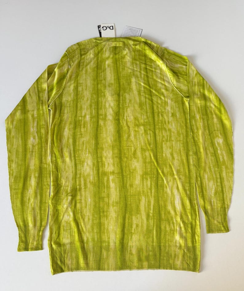 May include: A long-sleeved, lime green sweater with a vertical striped pattern. The sweater has a ribbed hem and cuffs, and a small tag is attached near the neckline. The fabric has a subtle sheen.