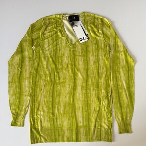May include: A lime green V-neck sweater with long sleeves. The sweater has a vertical striped pattern and a ribbed hem and cuffs. A tag with the "D&G" logo is attached to the neckline.