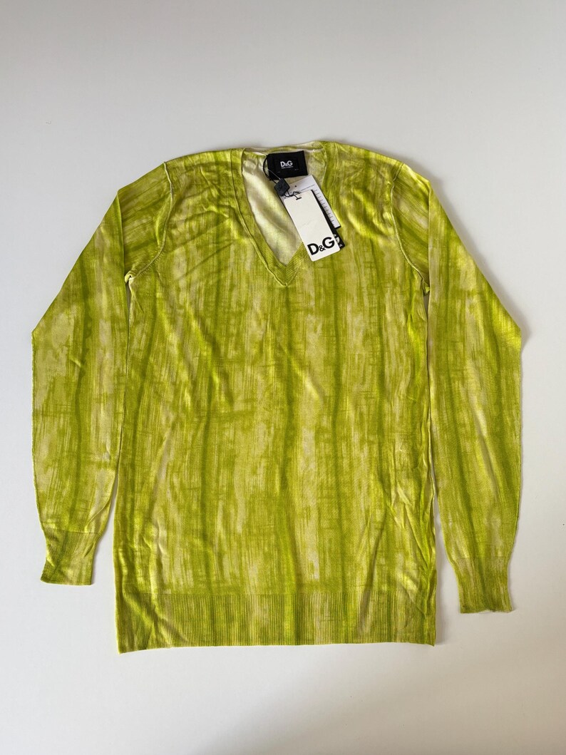 May include: A lime green V-neck sweater with long sleeves. The sweater has a vertical striped pattern and a ribbed hem and cuffs. A tag with the "D&G" logo is attached to the neckline.