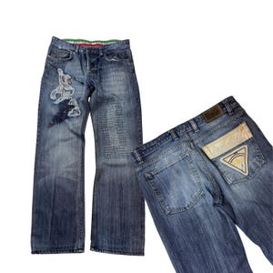 May include: Two pairs of blue denim jeans. One pair features an embroidered design on the front and a button fly. The other pair has a D&G label on the back pocket with a decorative patch.