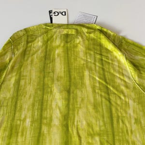 May include: A long-sleeved, lime green shirt with a vertical, textured pattern. The shirt has a crew neck and a tag from the brand D&G. The fabric has a subtle sheen, and the overall look is lightweight and airy.