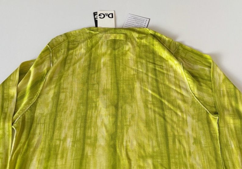 May include: A long-sleeved, lime green shirt with a vertical, textured pattern. The shirt has a crew neck and a tag from the brand D&G. The fabric has a subtle sheen, and the overall look is lightweight and airy.