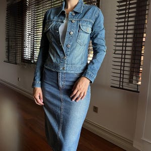 Puede incluir: Conjunto de chaqueta y falda vaquera en azul claro. La chaqueta tiene cierre de botones, bolsillos en el pecho y mangas largas. La falda es de largo midi, de estilo entallado. Un conjunto clásico y casual.