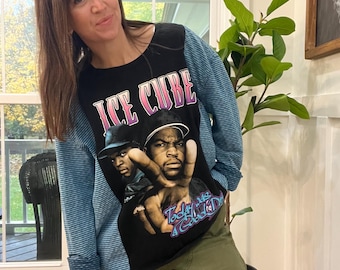 May include: Black long-sleeve shirt with a graphic of Ice Cube and the text "Ice Cube" in pink and purple. The shirt has blue striped sleeves and is paired with olive green cargo pants.