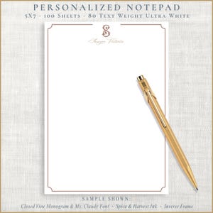 May include: Personalized notepad with a white interior and a decorative border. The notepad is 5x7 inches and includes 100 sheets of 80 text weight ultra white paper. A gold pen rests on the notepad. The notepad features a monogram and the name "Sawyer Victoria".