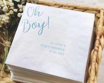 May include: A stack of white paper napkins with a diamond pattern. The napkins have the text "Oh Boy!" in light blue script, along with "ELAINE'S BABY SHOWER 02.05.2025". The napkins are in a woven basket.