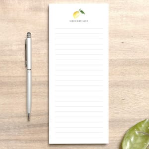 May include: A white grocery list notepad with a lemon illustration and the text "Grocery List" at the top. The notepad has lined paper for writing.
