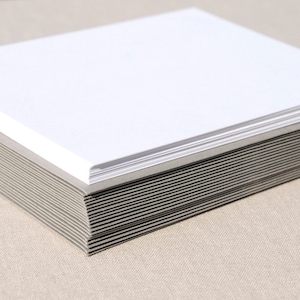 May include: A stack of blank white cards with gray backing. The cards are stacked neatly and are ready to be used for writing or crafting.