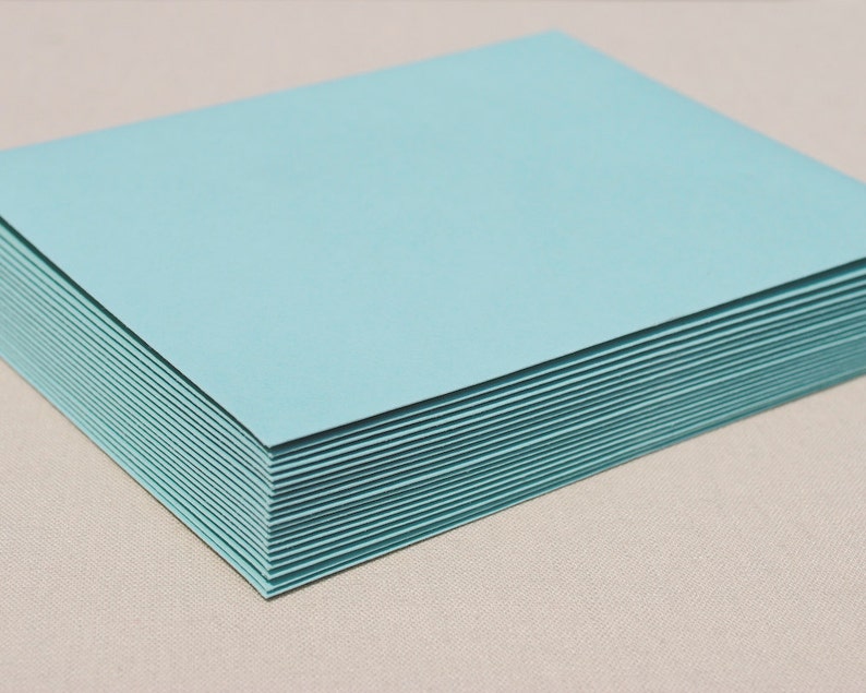 May include: A stack of light blue cardstock paper. The paper is smooth and has a subtle sheen.