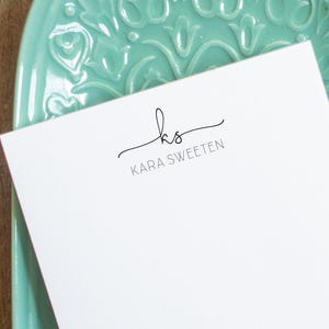 A custom notepad printed with script initials and all-caps name in black ink.