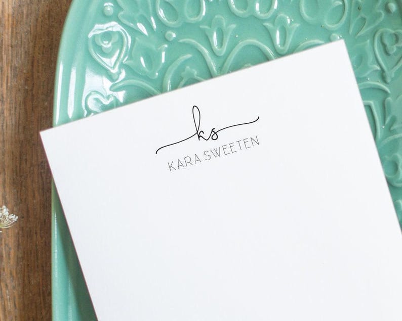 A custom notepad printed with script initials and all-caps name in black ink.