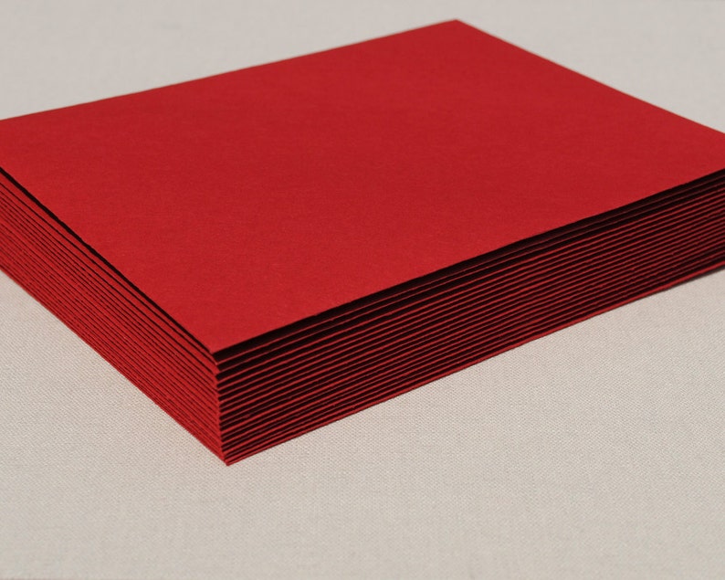 May include: A pile of vibrant red paper, possibly for stationery or crafting. The edges of the paper are visible, indicating the stack's depth. The paper has a smooth, matte surface.