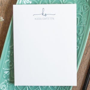 A custom notepad printed with script initials and all-caps name in blue ink.