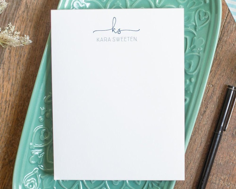 A custom notepad printed with script initials and all-caps name in blue ink.