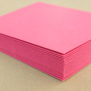 May include: A stack of pink cardstock paper. The paper is smooth and has a slight sheen.