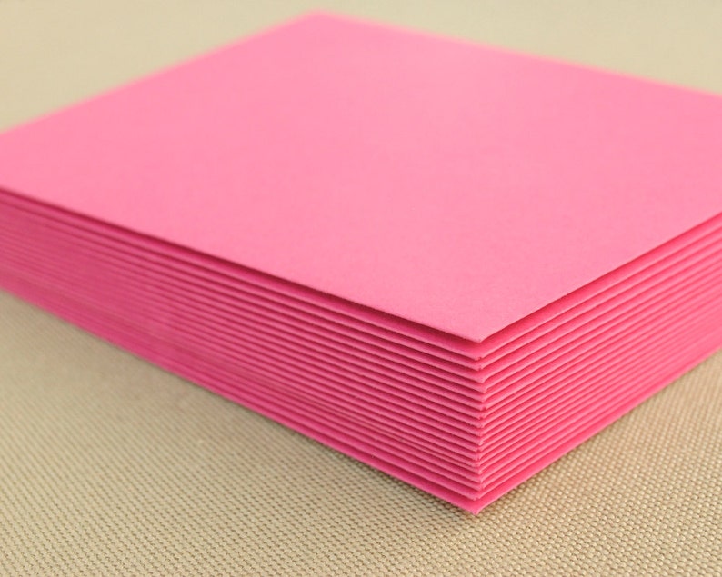 May include: A stack of pink cardstock paper. The paper is smooth and has a slight sheen.