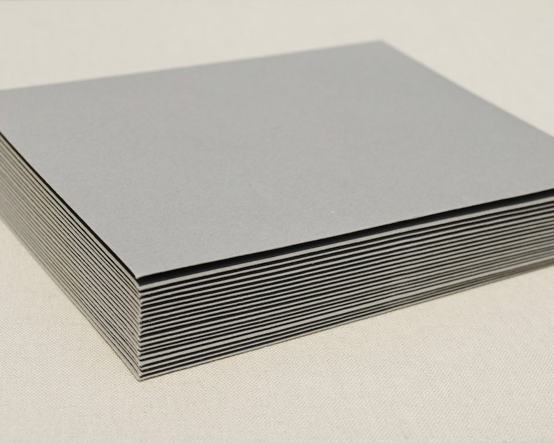 May include: A stack of gray cardstock paper. The paper is smooth and has a slight sheen.