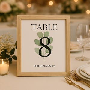 May include: A framed table number eight sign with a botanical design. The sign has the word "TABLE" at the top, the number eight in the center, and the text "PHILIPPIANS 4:6" at the bottom. The sign is surrounded by candles, flowers, and wine glasses.