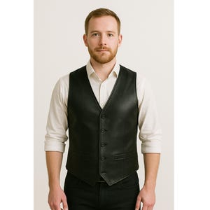 May include: A black leather vest with a V-neck and button closure. The vest has two front pockets and is worn over a white collared shirt. The person is wearing black pants.